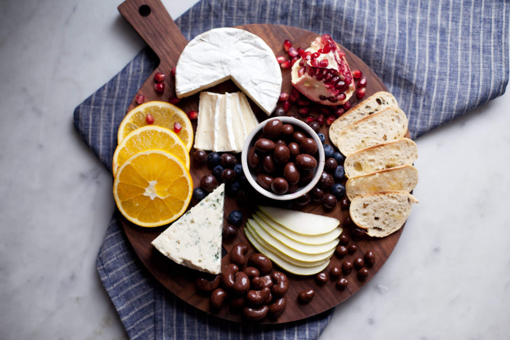 Cheese board with grapes, orange slices, and a variety of chocolates