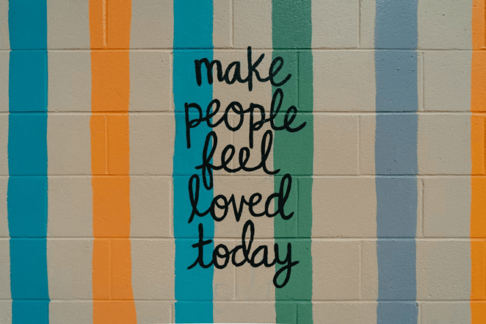 A cinderblock wall painted with cheerful colors and a handwritten message that says 
