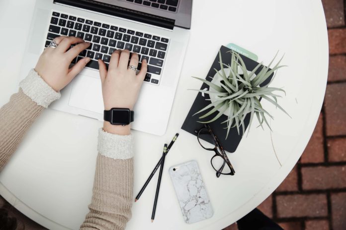 An employee logging in to a remote work day with nearby office supplies and a plant nearby.