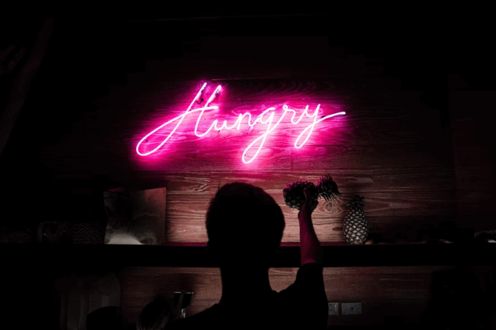 A neon sign in a dark bar, spelling out "Hungry" in looping cursive.