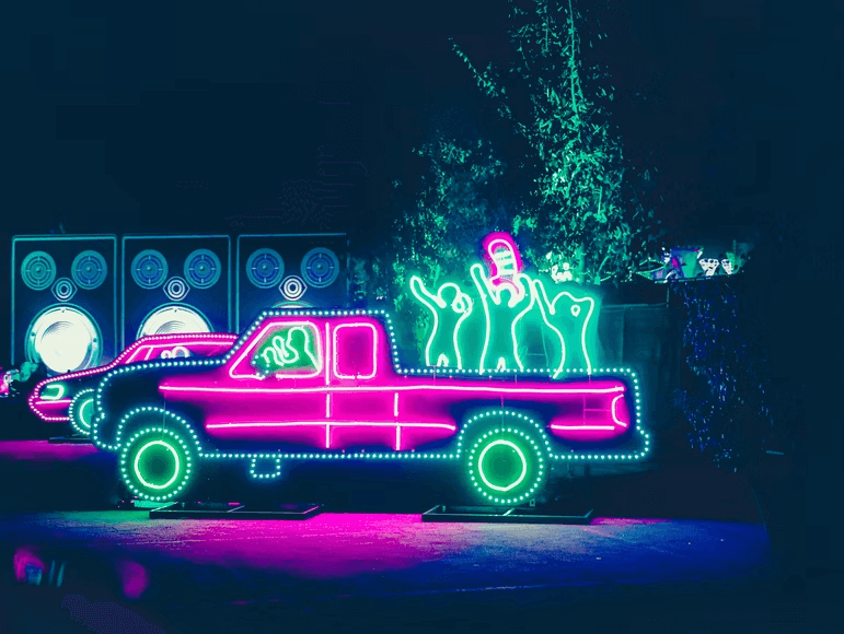 A neon display of a truck with people celebrating and dancing to music.