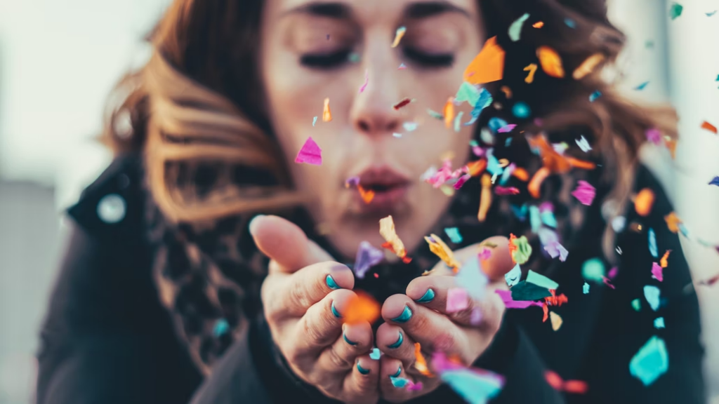 A woman celebrating by blowing a heap of confetti into the air. 