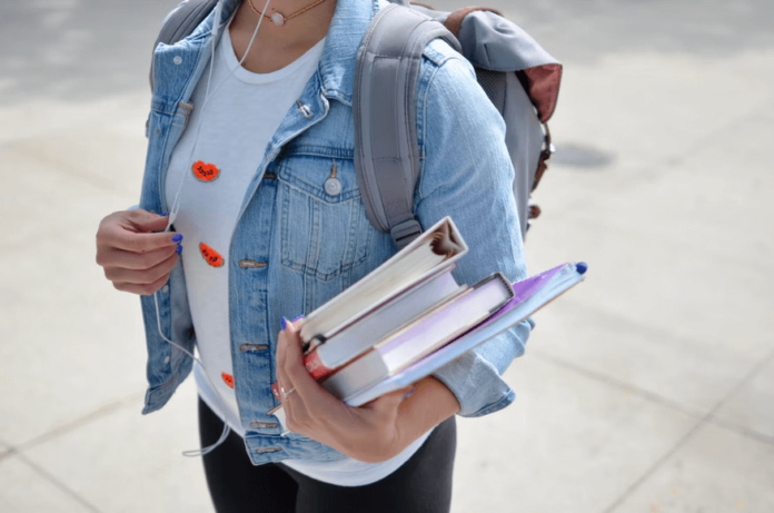 A college student carrying books and a backpack ready for class.