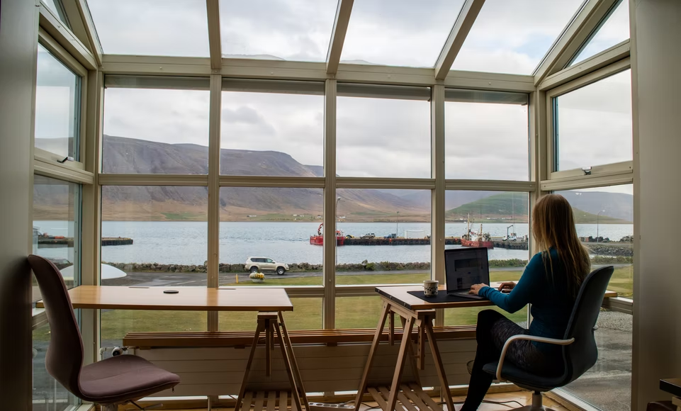 A woman working from a remote location with a beautiful view of the mountains and water.
