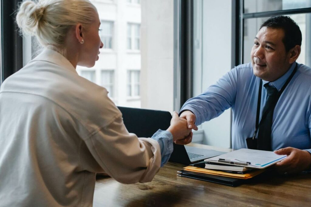 Two people in a professional setting coming to an agreement and shaking hands.