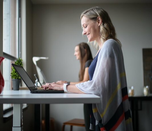16 Ways to Celebrate Employee Appreciation Day A woman smiling on her laptop at her standing desk.