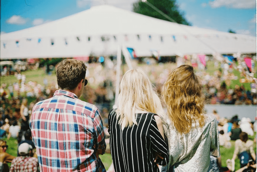 Young people at an outdoor festival sitting down and enjoying the view with snacks. 