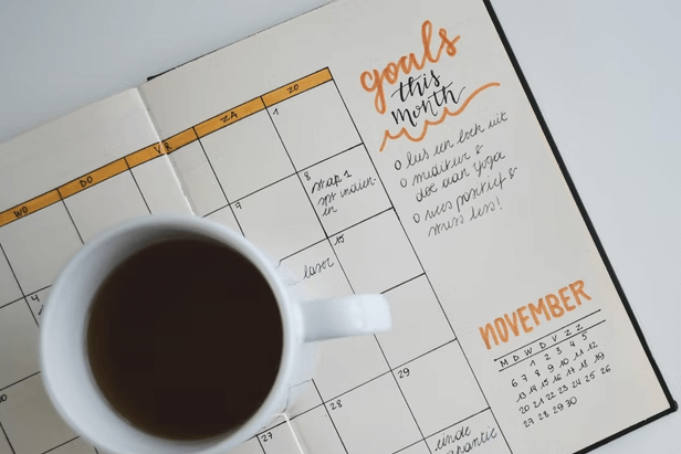 A day planner with important dates and goals outlined with a fresh cup of black coffee.