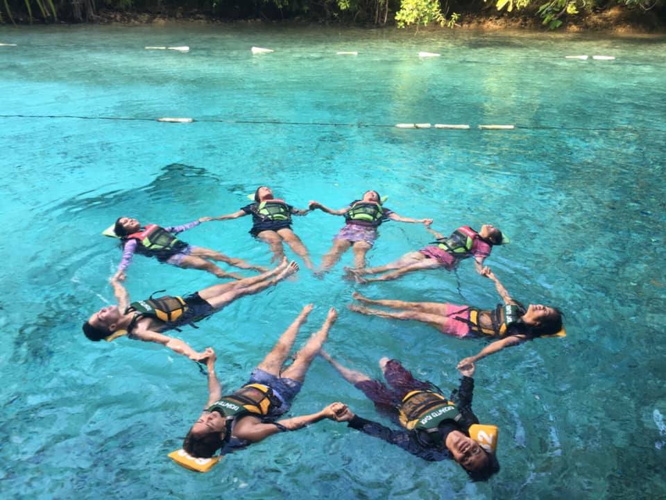Group of friends floating in clear blue water in a star formation.