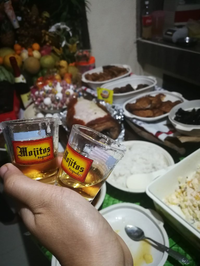 Two celebratory shots in the foreground with a spread of traditional Filipino Birthday foods in the background.